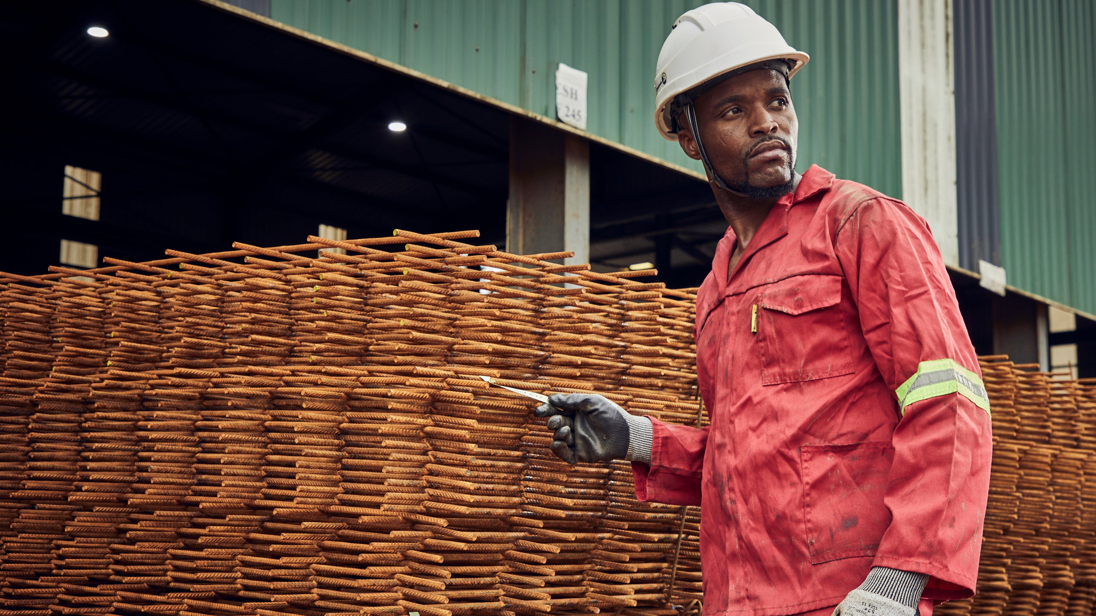 Worker in red uniform and hard hat standing next to stacked wooden crates with a brand logo in the corner.slider_item_daKWRh