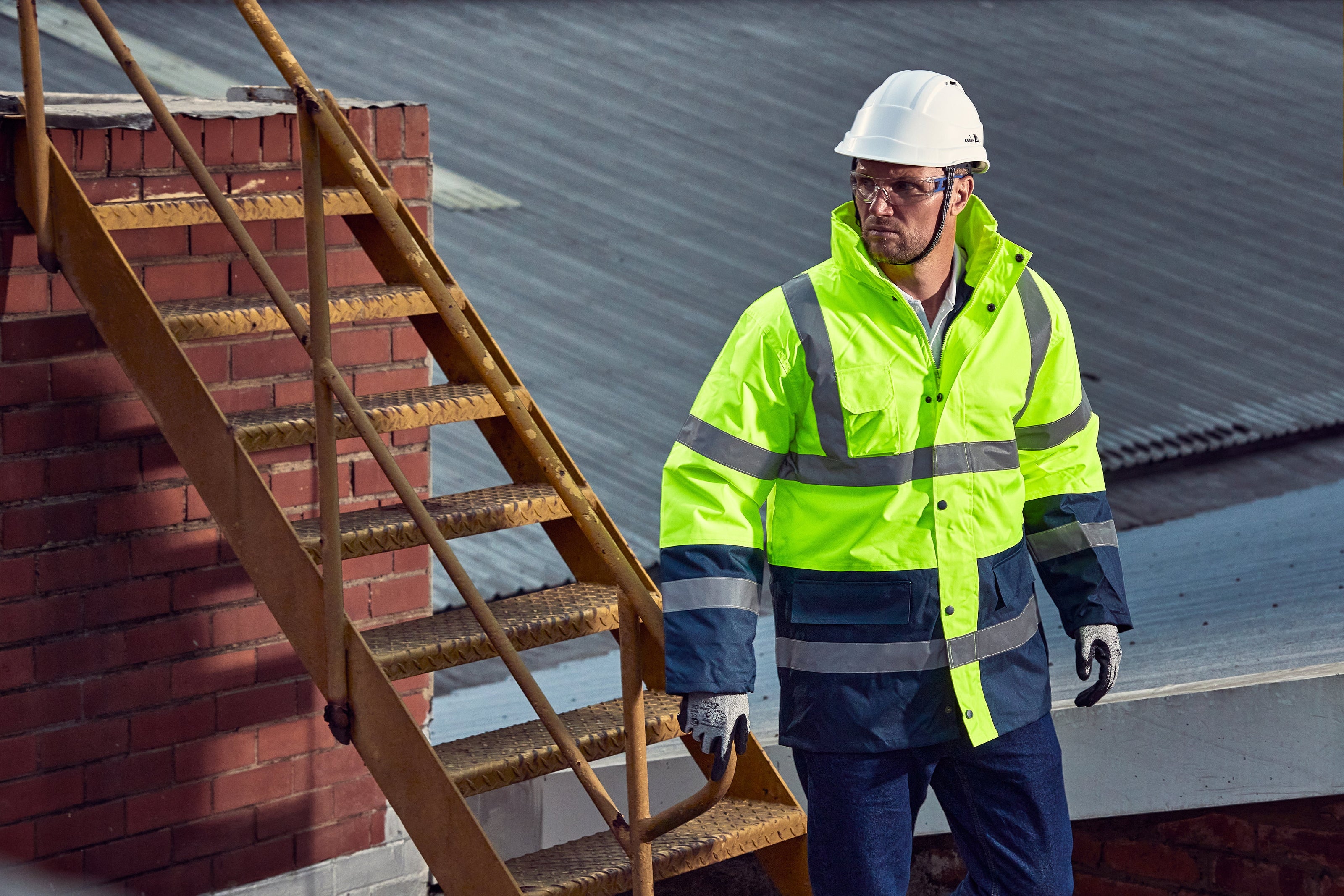 Person in safety gear walking on a roof with a ladder
