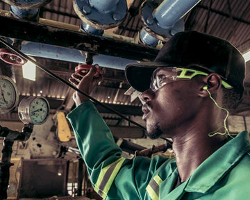 Person in a green uniform and hard hat working on machinery with 'Dromex' logo.